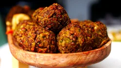 Des boulettes de lentilles rondes et dorées, piquées d'herbes vertes, empilées dans un bol en bois clair au grain apparent.